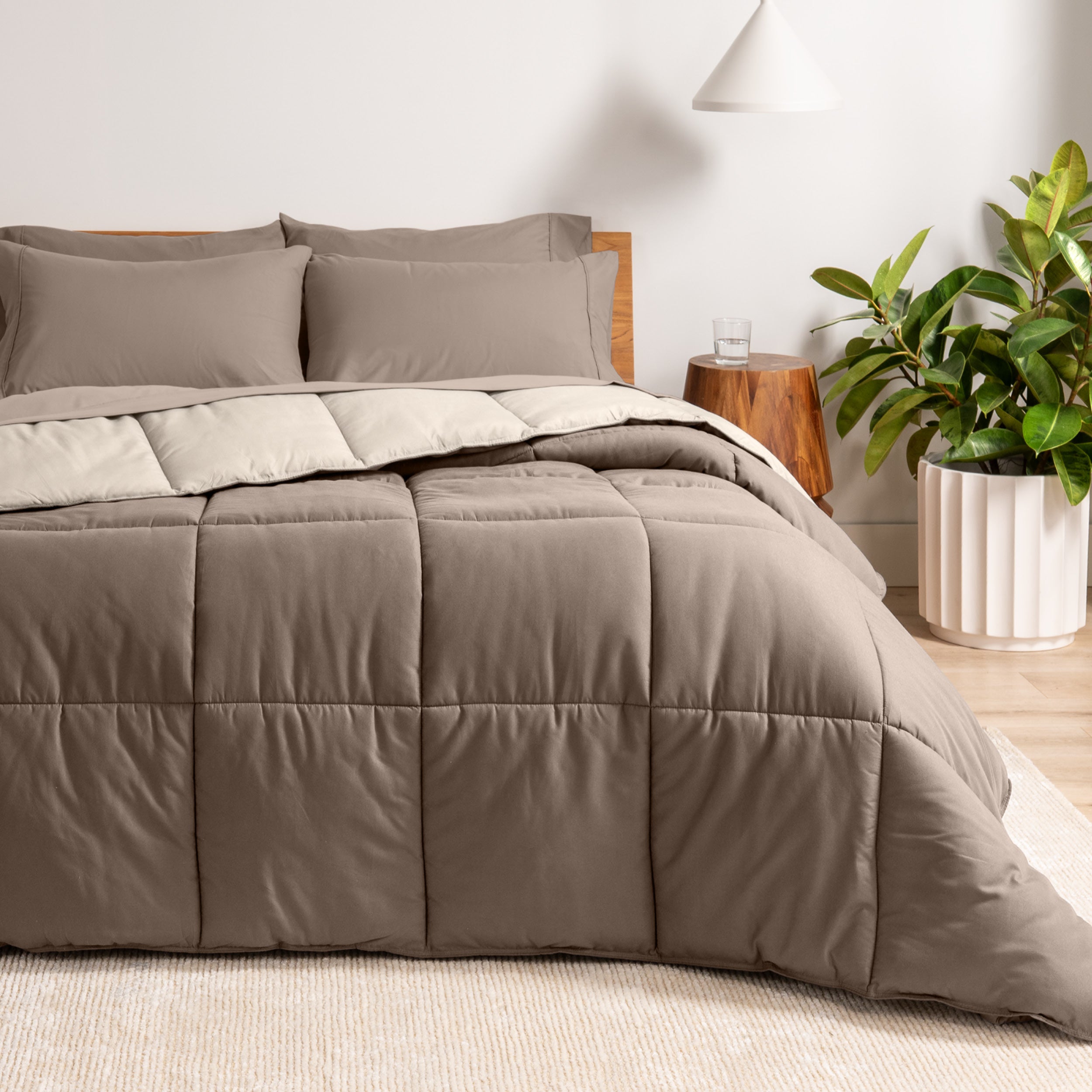 A wooden bed frame with a reversible comforter and sheet set on the mattress in a bright warm room.