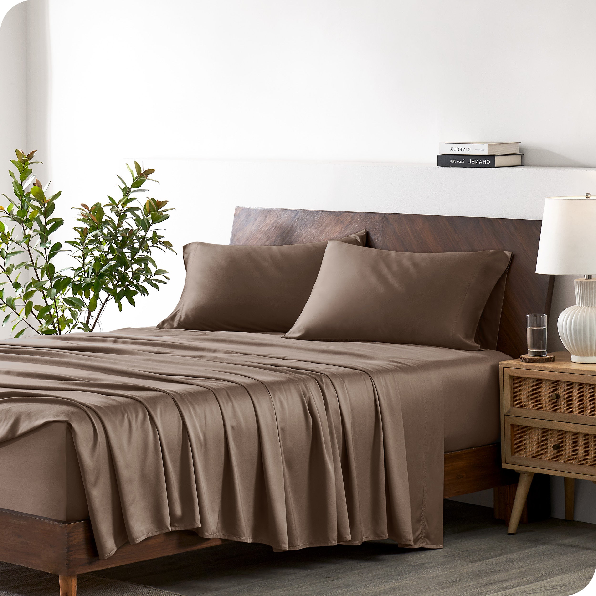 Modern bedroom with a bed against a white wall with a nightstand next to the bed. The bed has bamboo sheets draped over it.