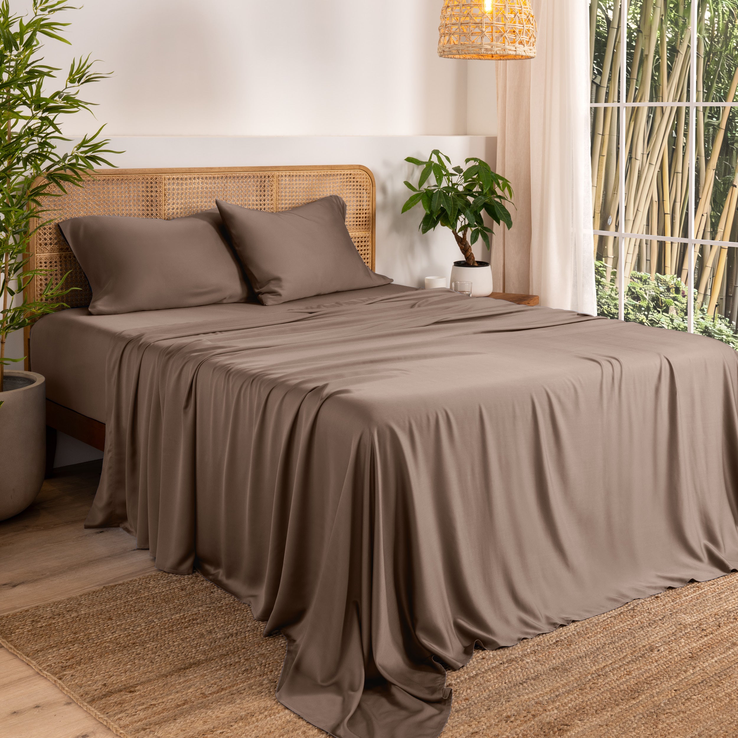 Bamboo sheets on a bed in a bedroom with plants and a window.