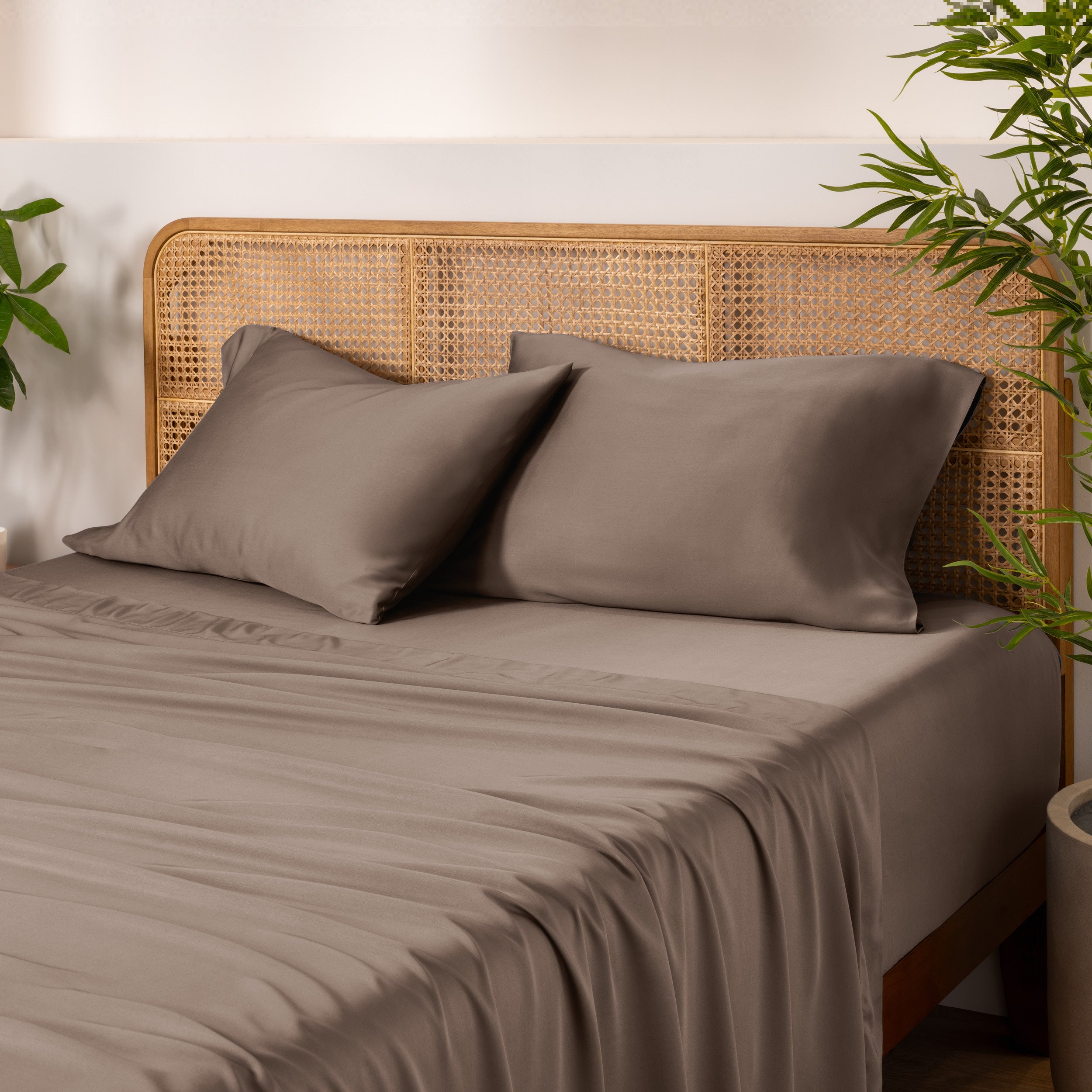 Bamboo bed sheets and pillowcases on a bed with a wicker headboard and plants in the background.