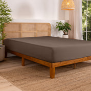 Bed with fitted sheet in a bedroom setting with plants and a lamp.