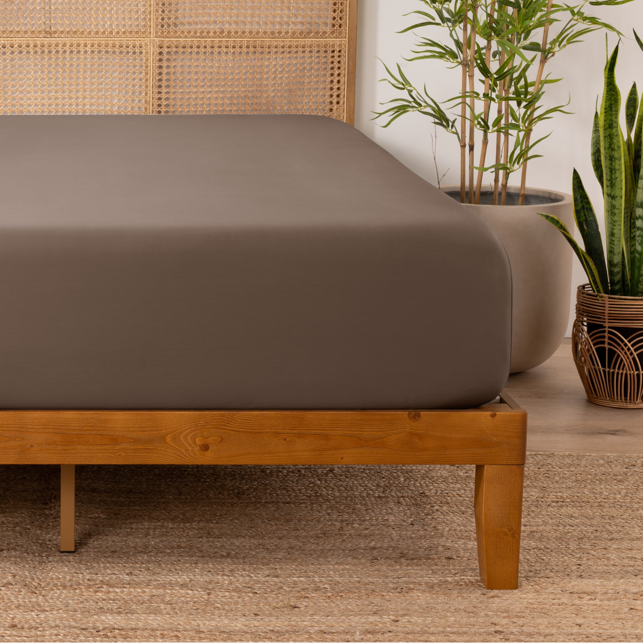 Bamboo fitted sheet on a wooden bed with plants in the background