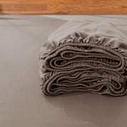 Folded fitted sheet on a bed with a wooden headboard.