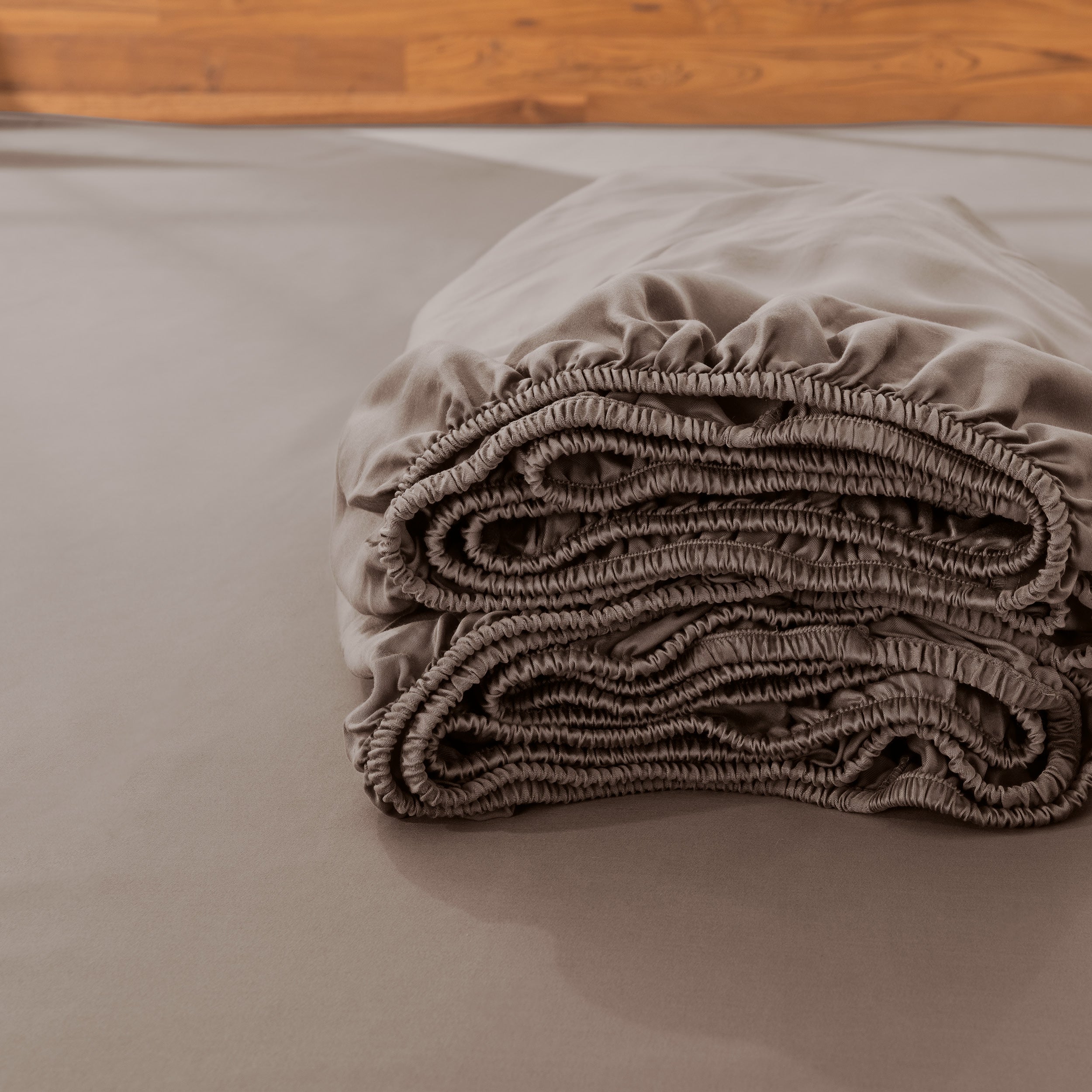 Folded fitted sheet on a bed with a wooden headboard.