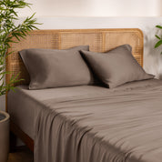Bamboo bed sheets and pillowcases on a bed with a wicker headboard in a room with plants.
