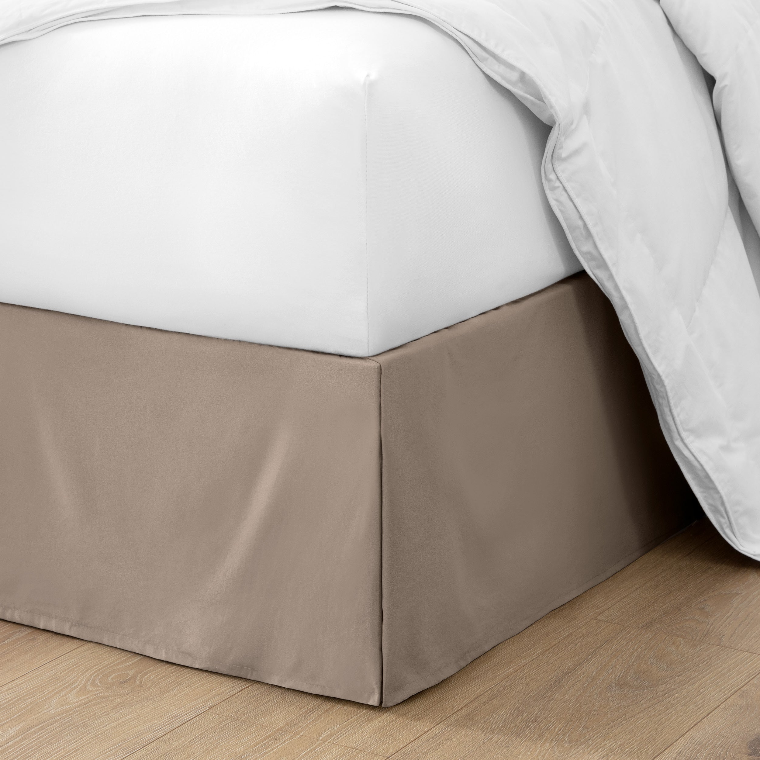 The corner of a bed with a bed skirt and comforter on it