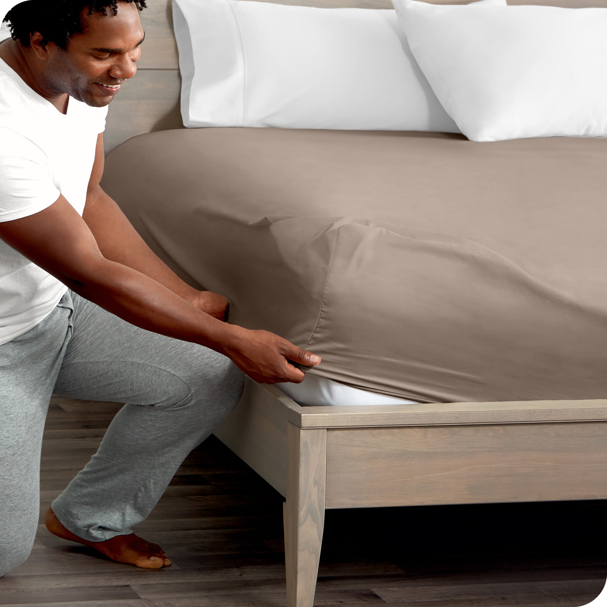 A man kneeling while putting a fitted sheet on a bed