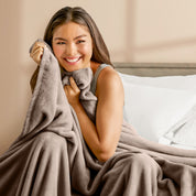 A woman sitting on a bed wrapped in a microplush blanket