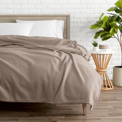 A polar fleece blanket on a bed next to a table and a large plant