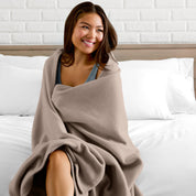 A woman sitting at the end of a bed with a fleece blanket wrapped around her shoulders