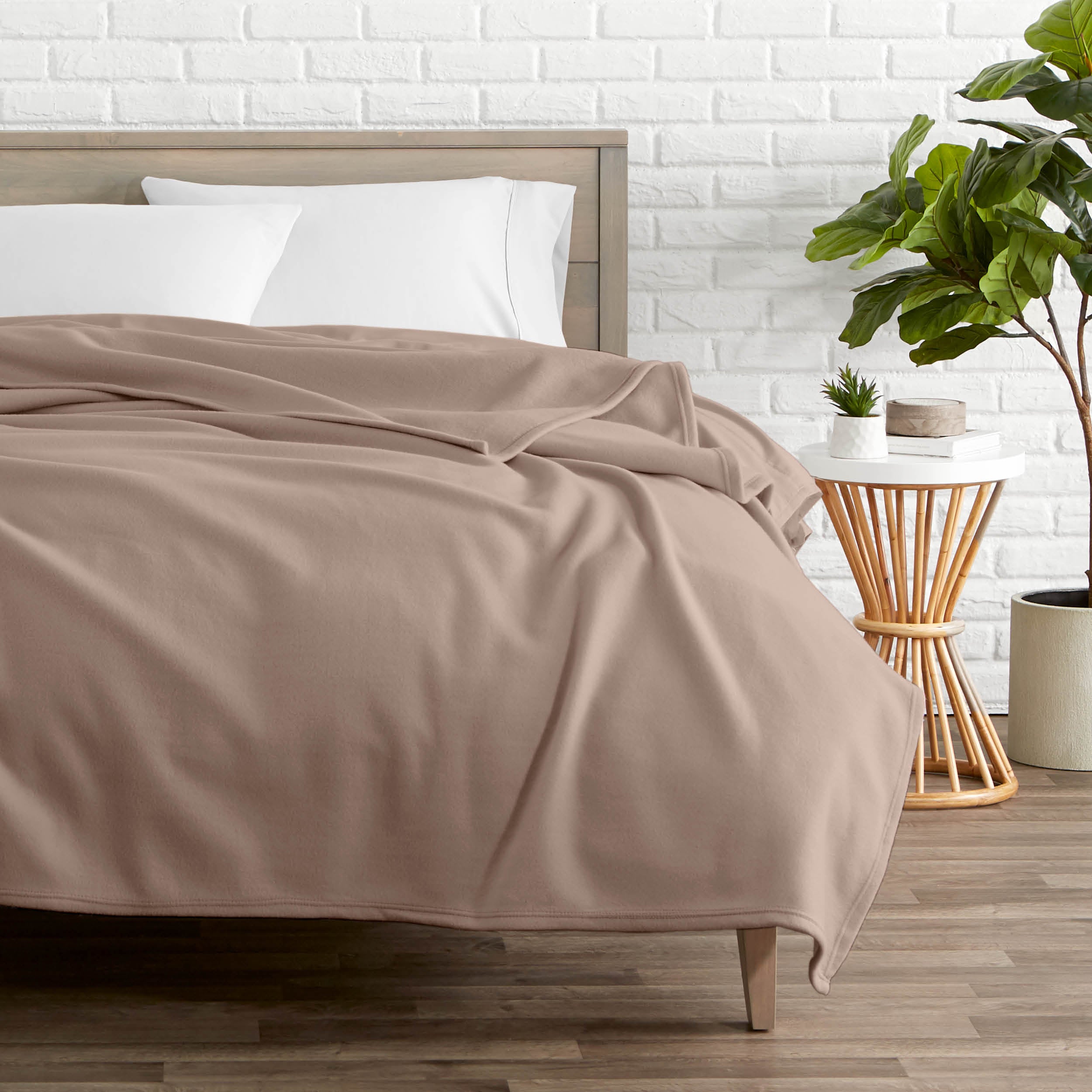A polar fleece blanket on a bed next to a table and a large plant