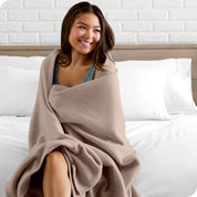 A woman sitting at the end of a bed with a fleece blanket wrapped around her shoulders