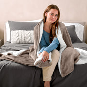 Woman cuddling with a sherpa blanket while sitting on the end of a bed