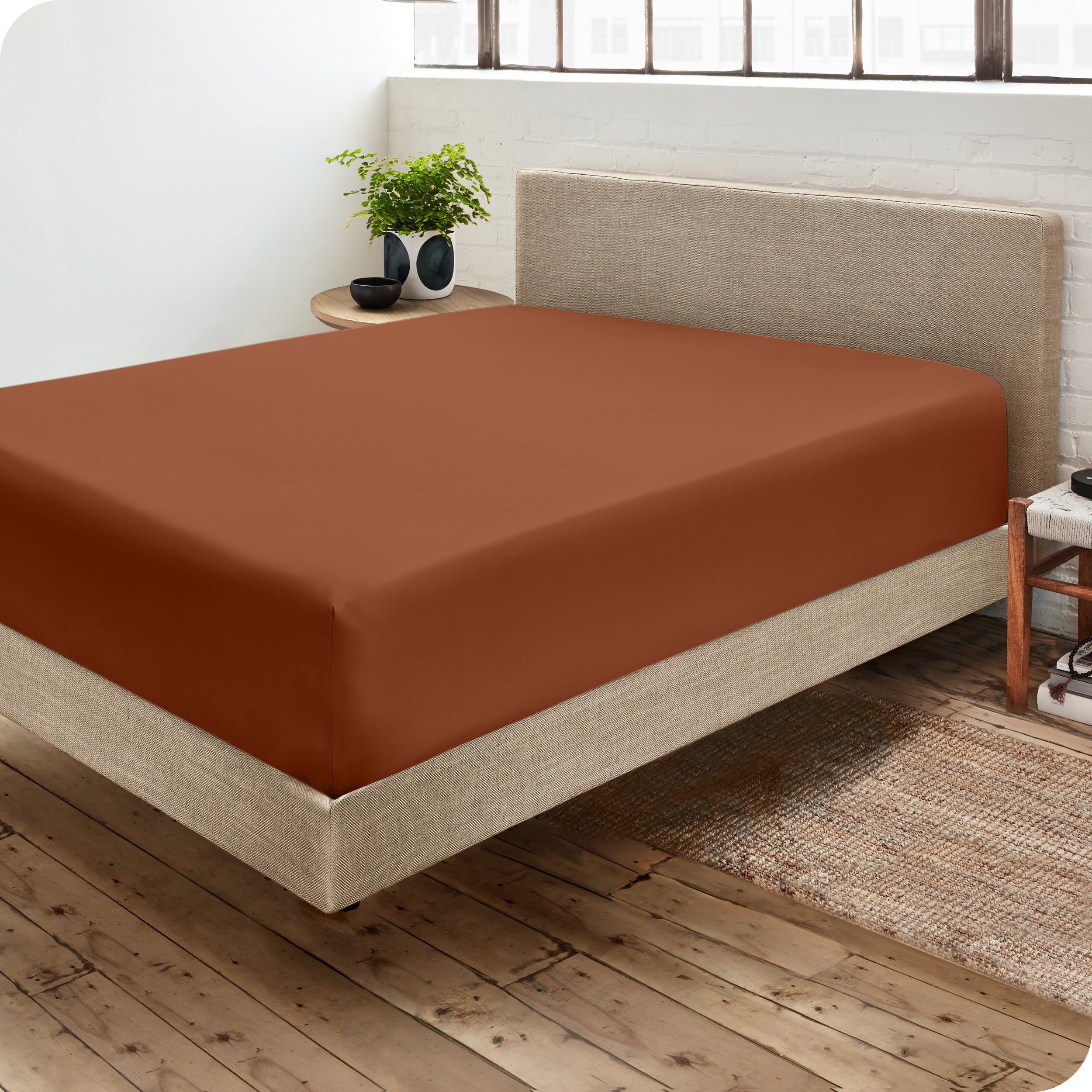 Corner view of a modern bed with a microfiber fitted sheet on the mattress. 