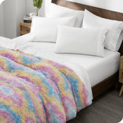 Diagonal view of a bed made with white sheets and pillowcases with a tie dye shaggy duvet cover on top