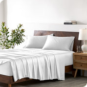 Modern bedroom with a bed against a white wall with a nightstand next to the bed. The bed has bamboo sheets draped over it.