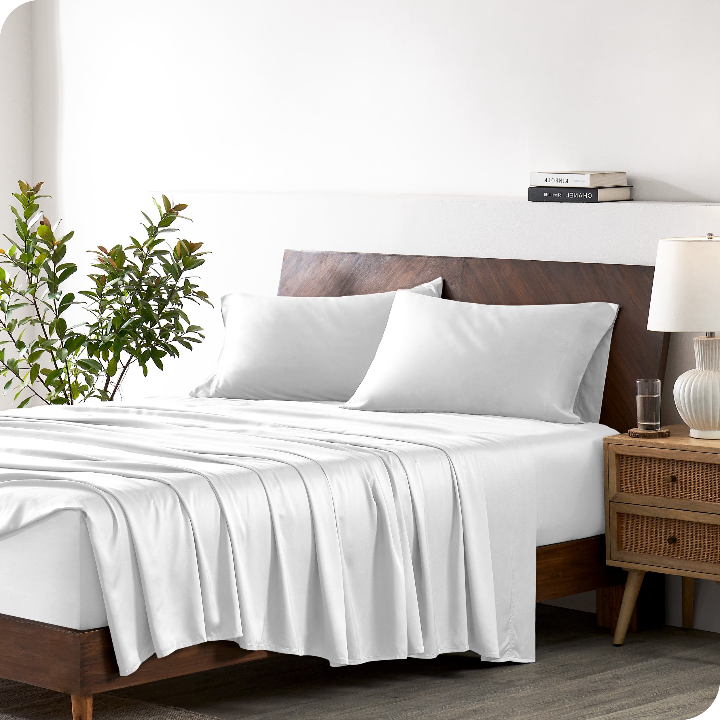 Modern bedroom with a bed against a white wall with a nightstand next to the bed. The bed has bamboo sheets draped over it.