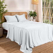 Bamboo sheets on a bed in a bedroom with plants and a window.
