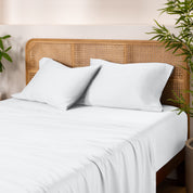 Bamboo bed sheets and pillowcases on a bed with a wicker headboard and plants in the background.