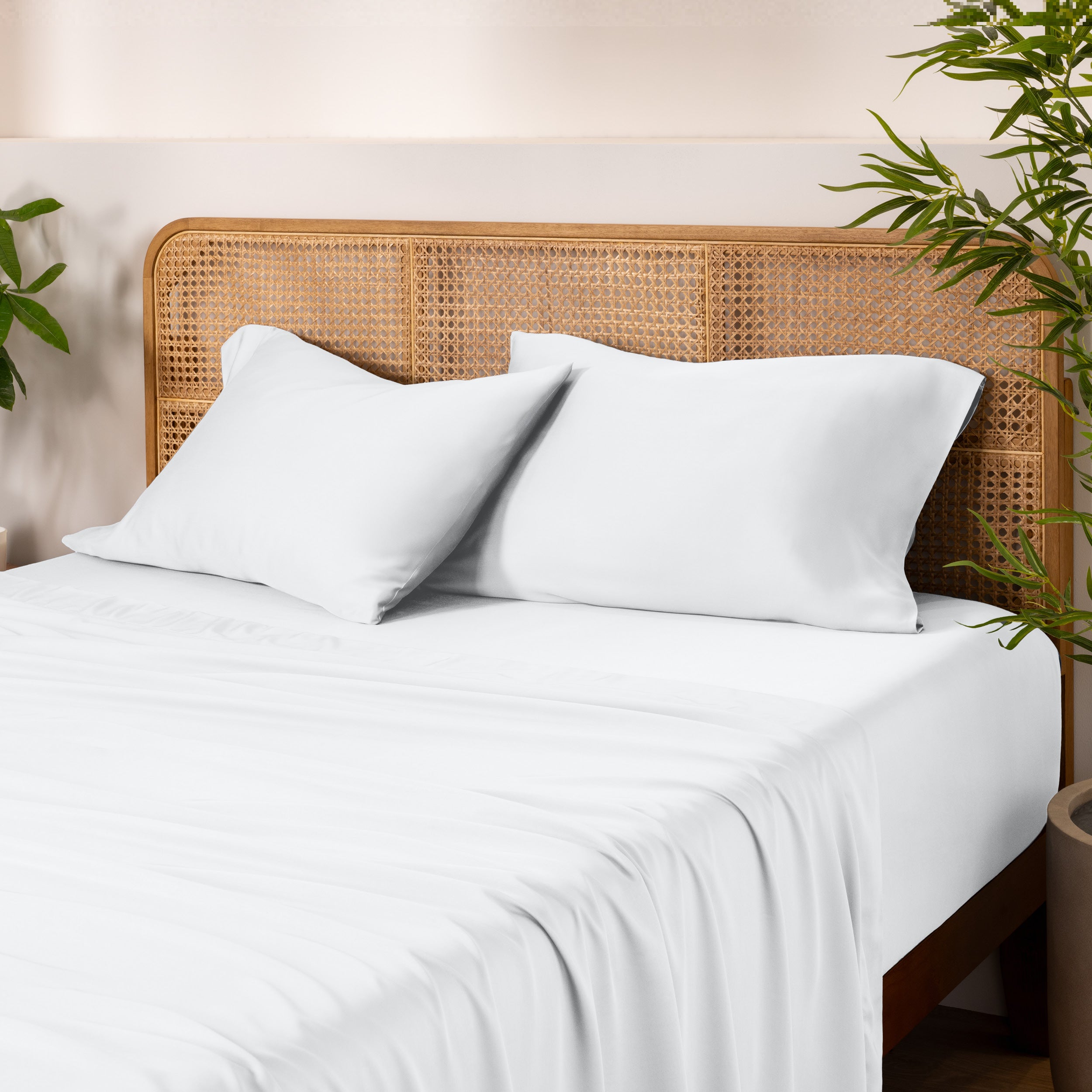 Bamboo bed sheets and pillowcases on a bed with a wicker headboard and plants in the background.