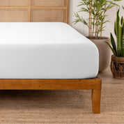 Bamboo fitted sheet on a wooden bed with plants in the background