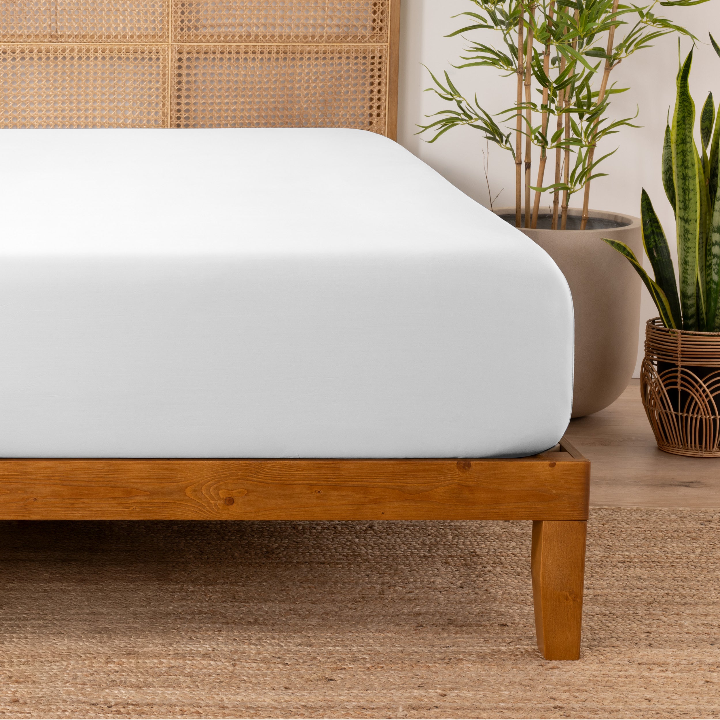 Bamboo fitted sheet on a wooden bed with plants in the background