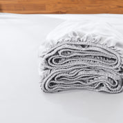 Folded fitted sheet on a bed with a wooden headboard.