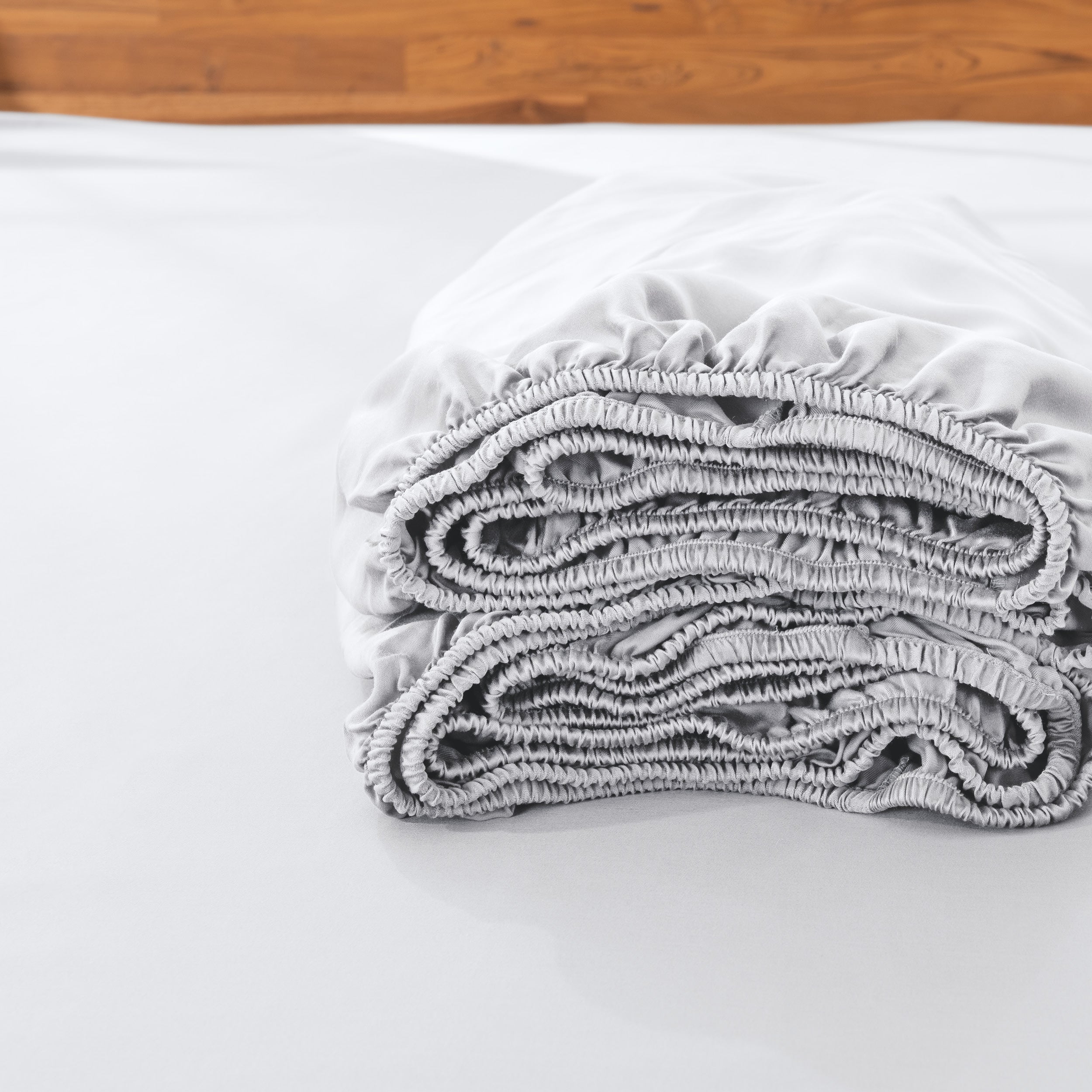Folded fitted sheet on a bed with a wooden headboard.