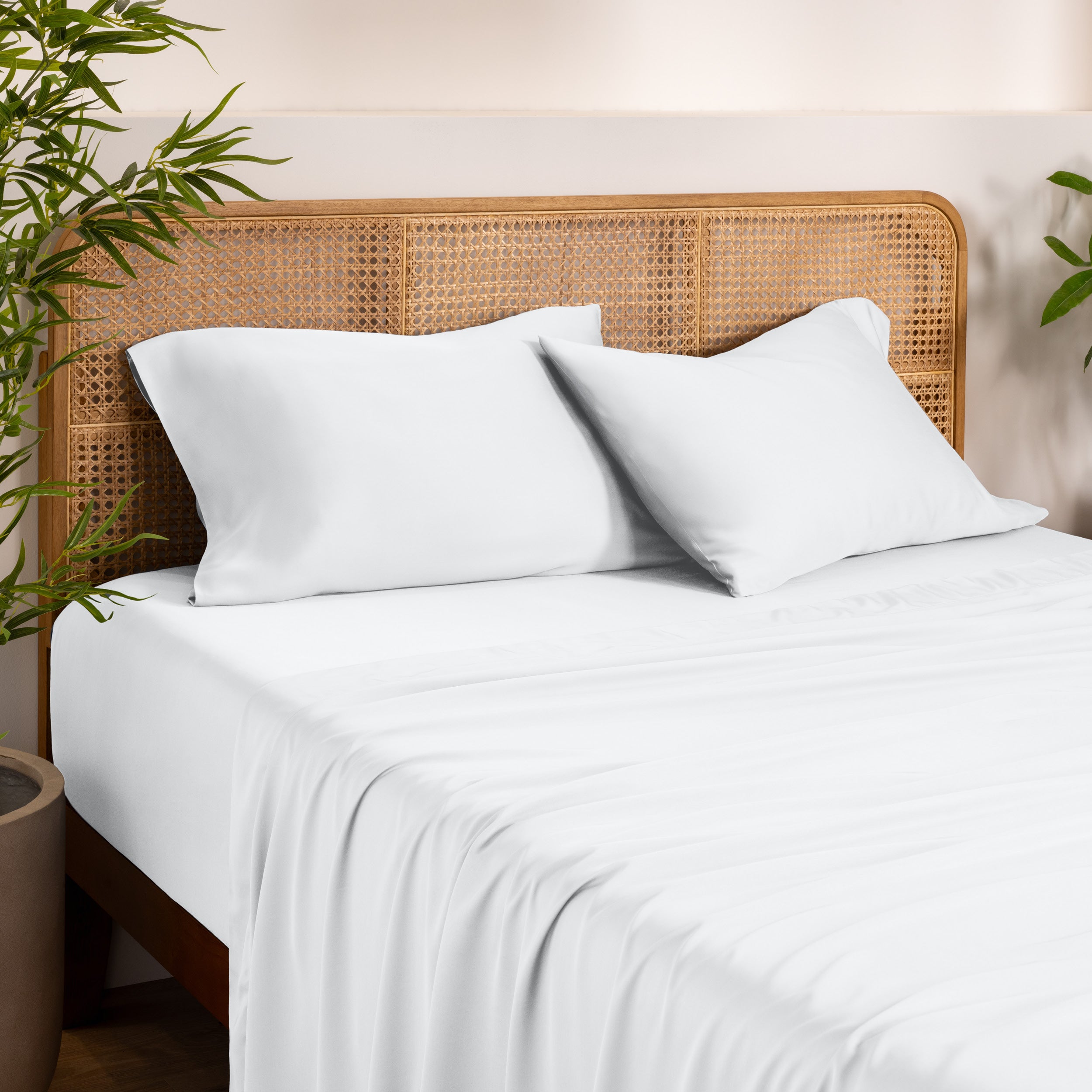 Bamboo bed sheets and pillowcases on a bed with a wicker headboard in a room with plants.