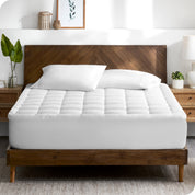 A modern bedroom with plants on the nightstands and a mattress pad on the bed