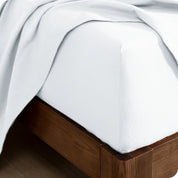 Close up of the corner of a mattress with a fitted sheet and flat sheet on it