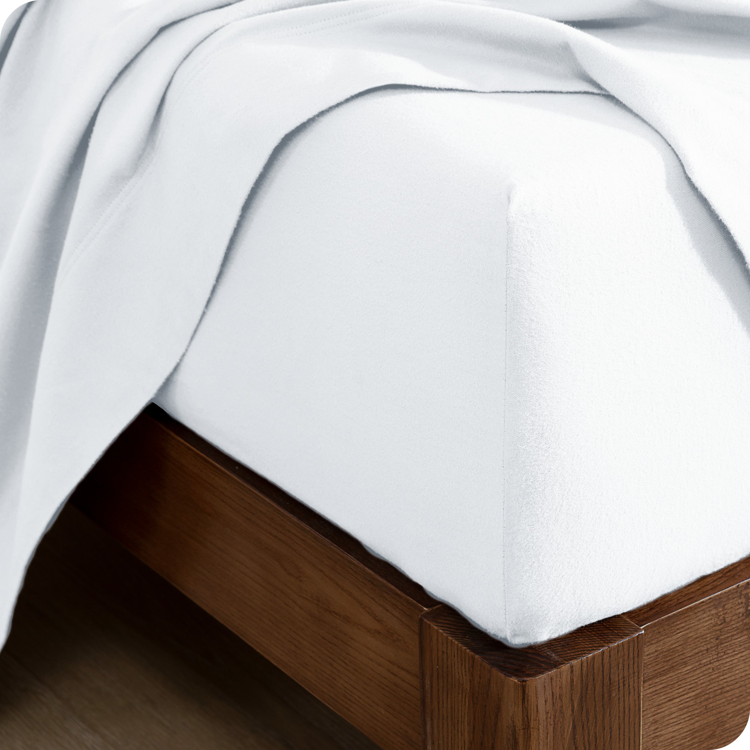 Close up of the corner of a mattress with a fitted sheet and flat sheet on it