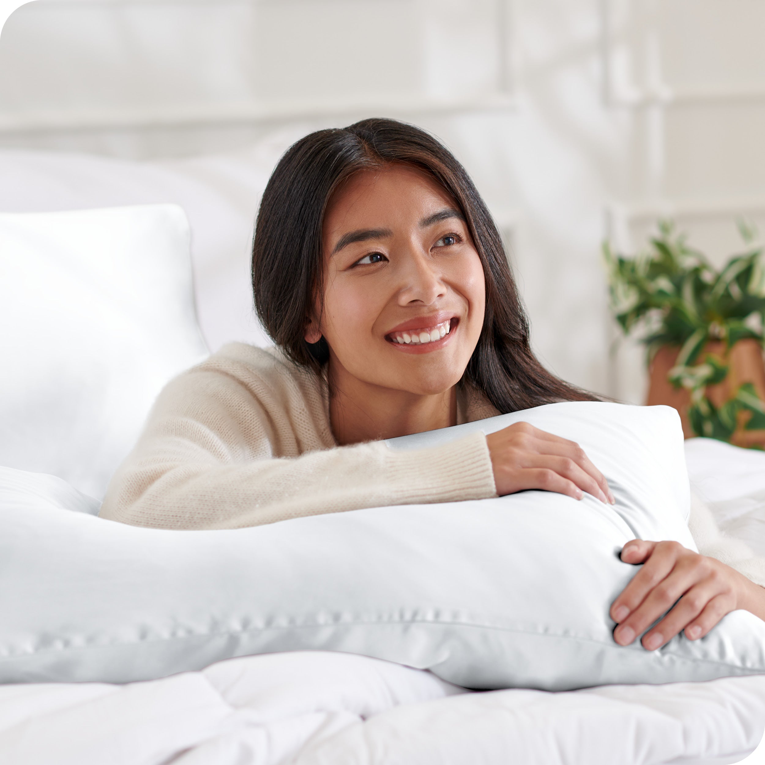 A woman on a bed resting her arm on a silk pillowcase covered pillow