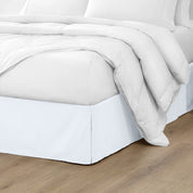 The corner of a bed with a bed skirt and comforter on it