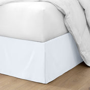 The corner of a bed with a bed skirt and comforter on it