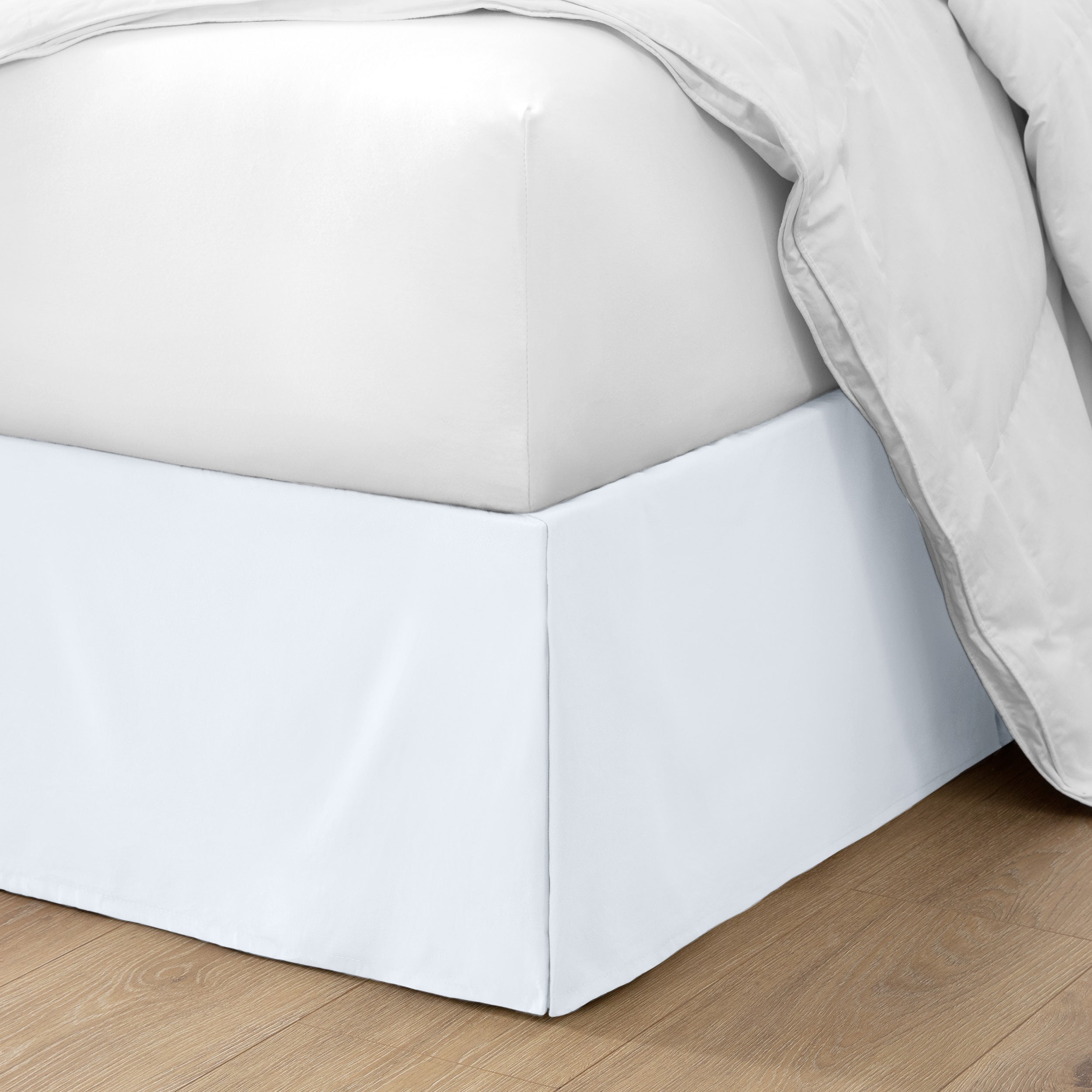 The corner of a bed with a bed skirt and comforter on it