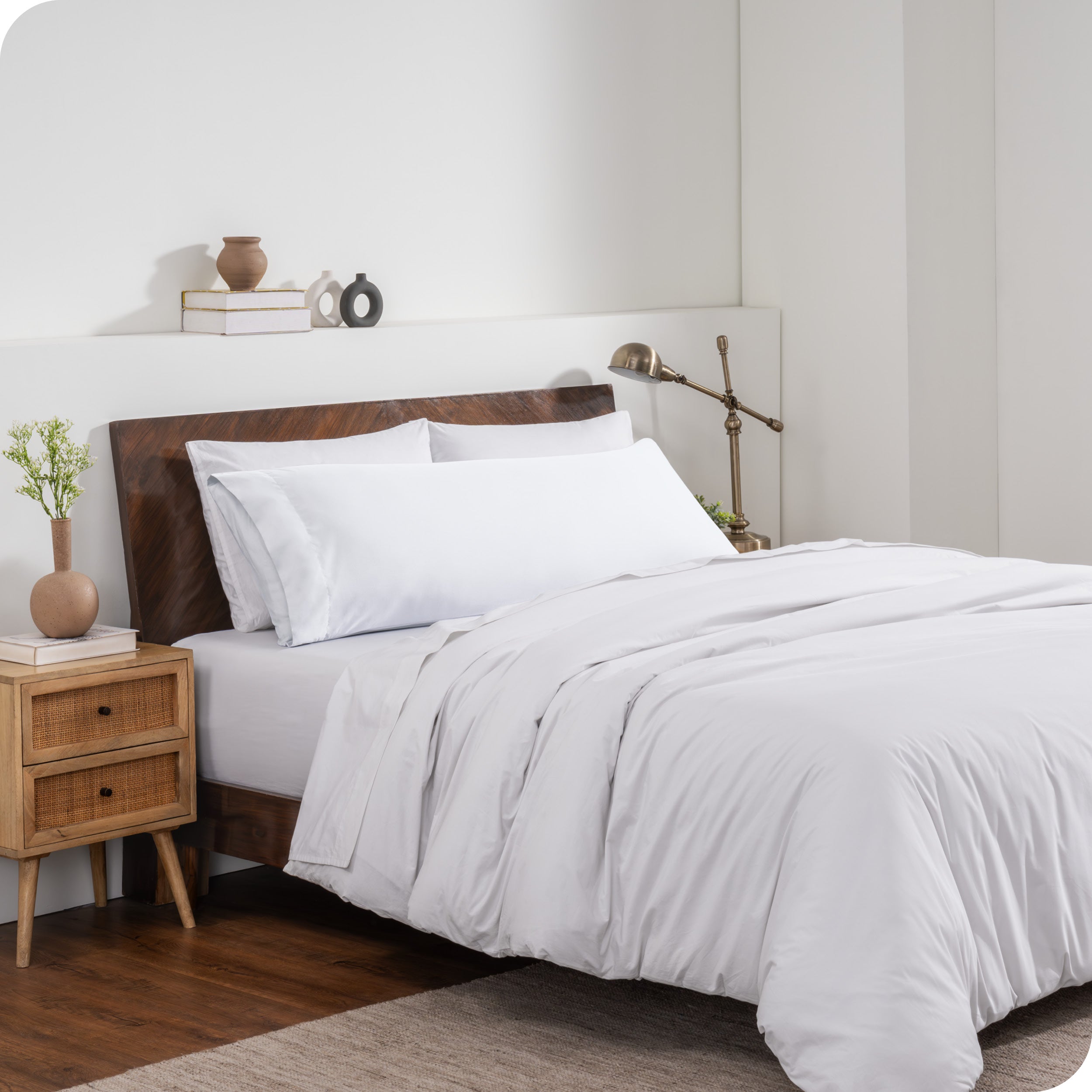 A body pillow cover on a pillow on a bed made with all white bedding