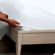 A man is kneeling while putting a fitted sheet on a mattress

