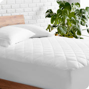 A modern bed with a wooden bed frame with a quilted mattress pad on.
