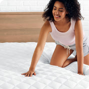 A woman is pushed her hand down on a quilted mattress pad on the bed