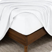 A corner of a mattress with a fitted sheet and a flat sheet on it.