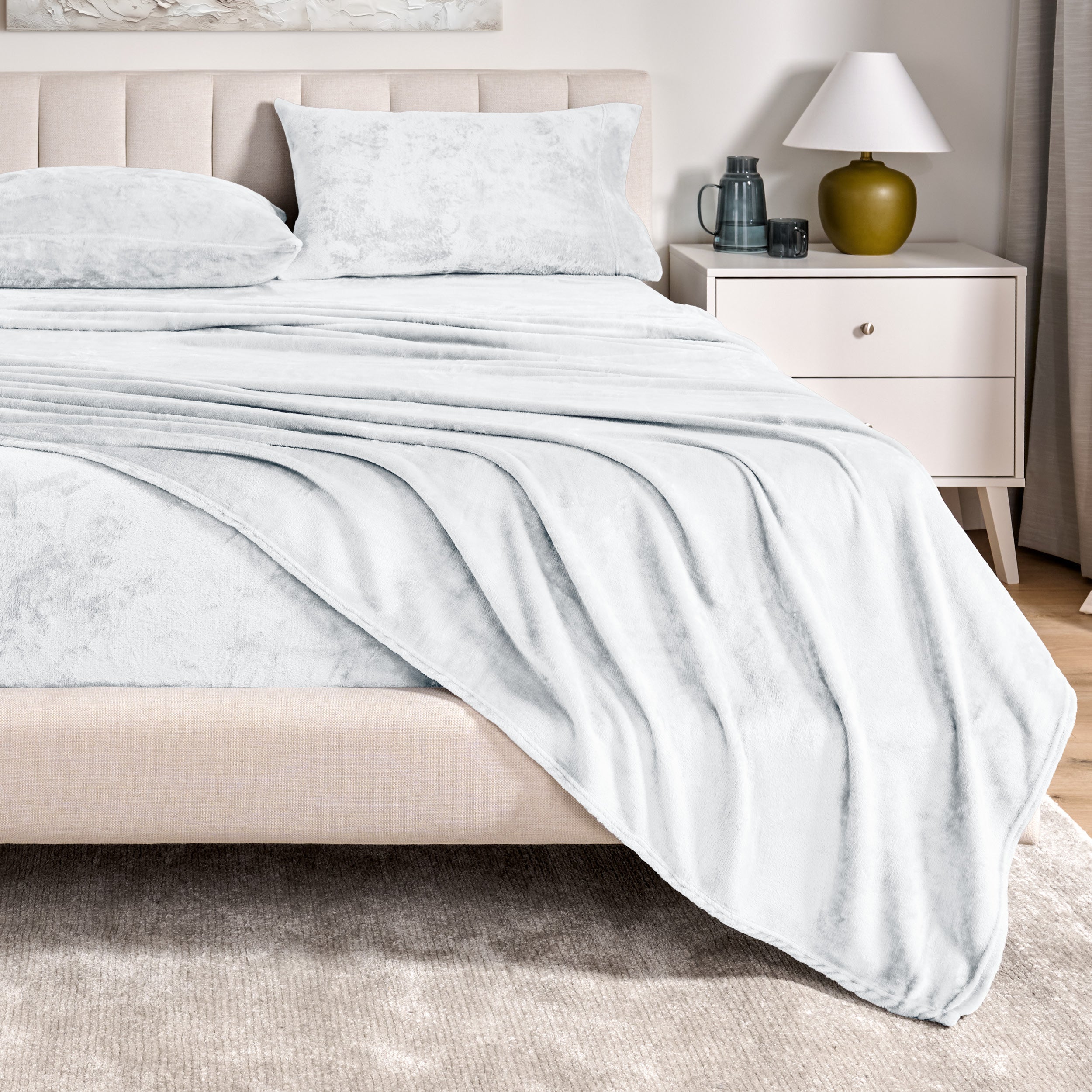 Microplush sheets on a bed in a bedroom setting with a nightstand and lamp.