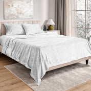 Sheets and matching pillowcases on a bed in a bedroom with a lamp and window in the background.