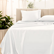 Organic sateen bedding on a bed with a beige headboard and plant in the corner.