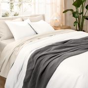 A woman sitting on a bed made with organic cotton sateen sheets and pillowcases