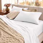 Neatly made bed with pillows and a beige blanket in a bright room.