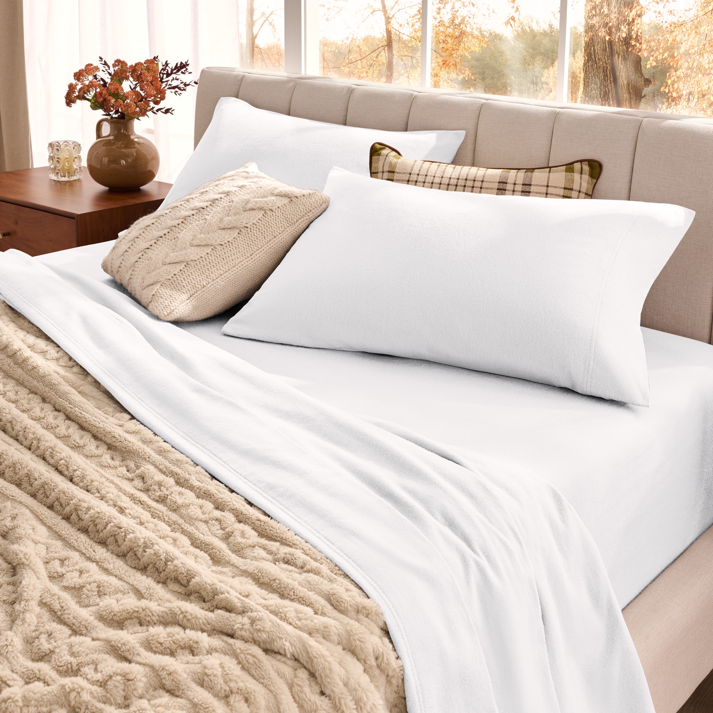 Neatly made bed with pillows and a beige blanket in a bright room.