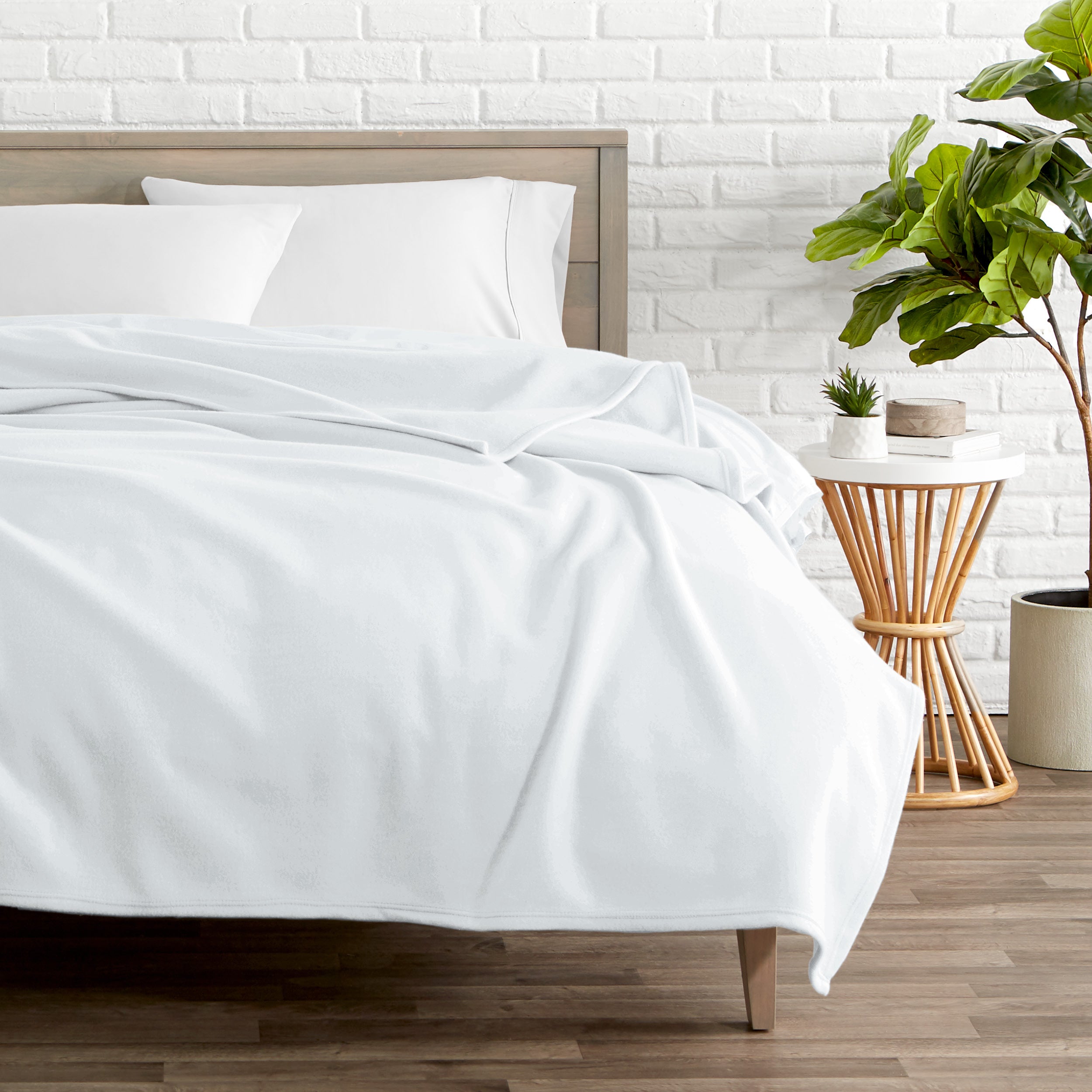 A polar fleece blanket on a bed next to a table and a large plant