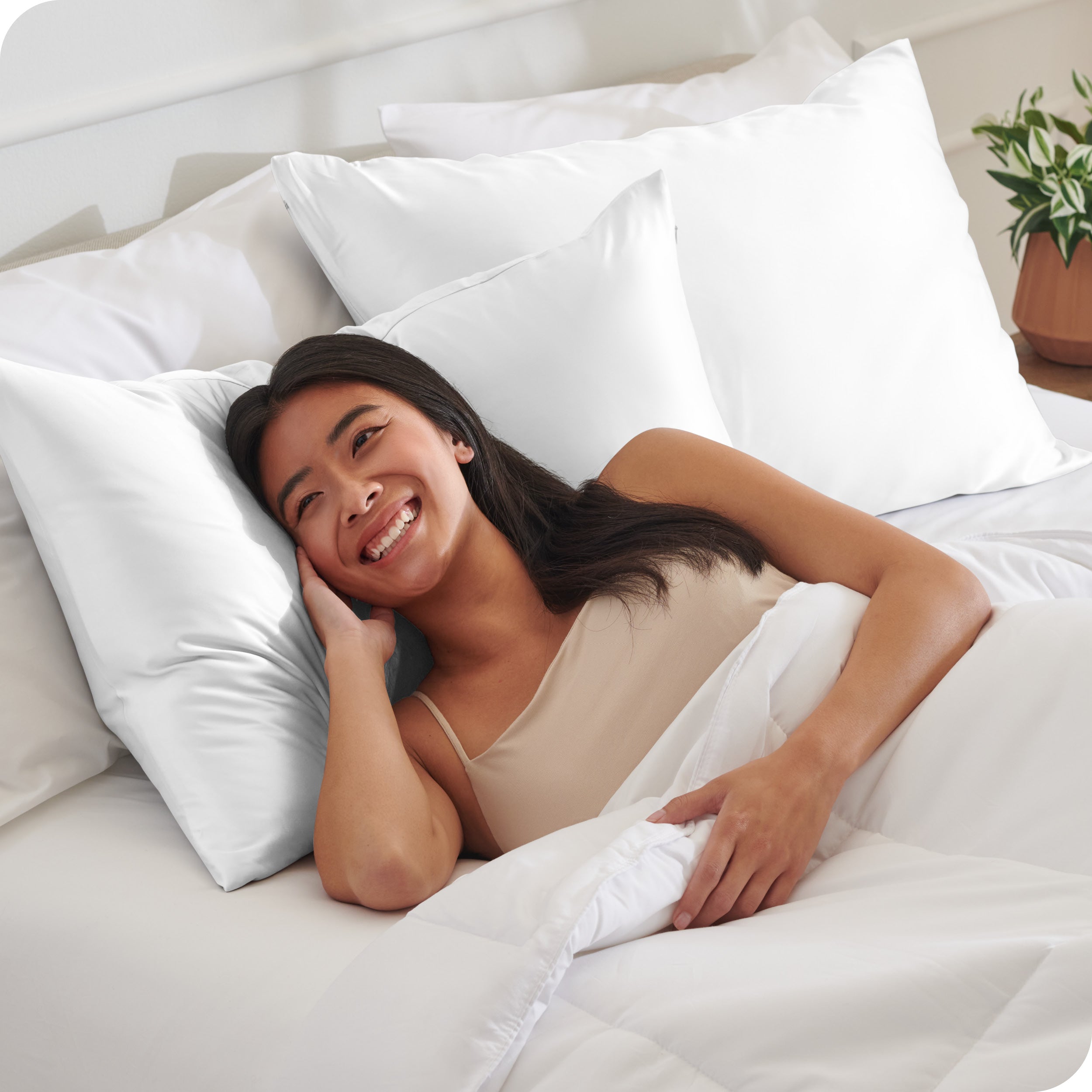 A woman in bed with her head resting on a silk pillowcase covered pillow