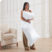 A woman standing while holding 2 pillows with silk pillowcases